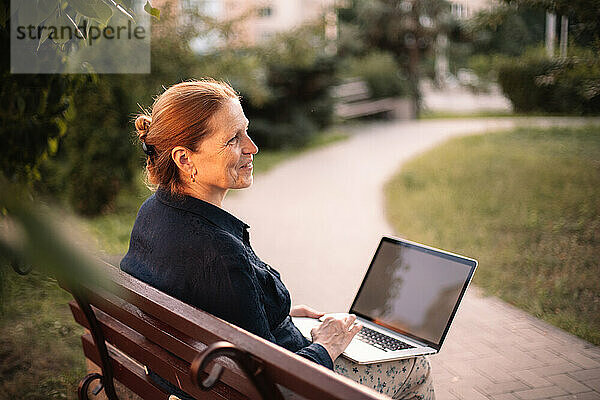 Glückliche reife Geschäftsfrau mit Laptop-Computer auf Bank sitzend