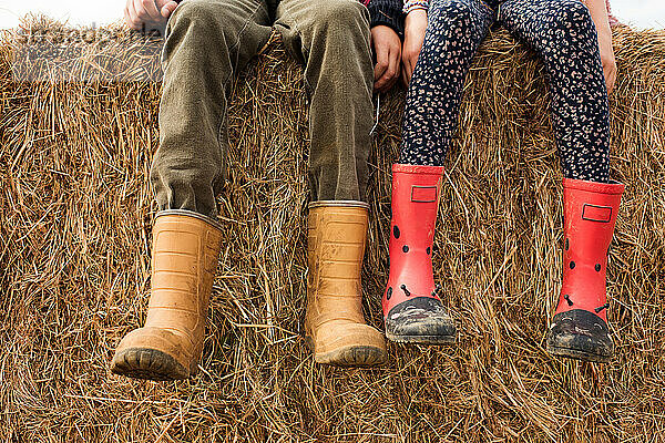 zwei Kinderfüße und Gummistiefel auf einem Heuballen