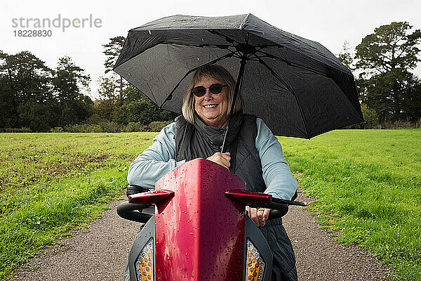 Rentnerin mit Behinderung auf einem Elektroroller draußen im Regen