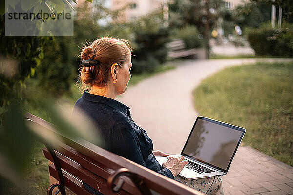 Reife Geschäftsfrau sitzt mit Laptop auf Bank im Park