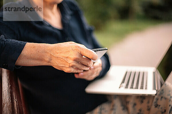 Mature business woman using smart phone and laptop computer in park