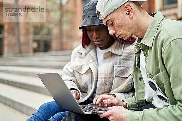 Fröhliche multiethnische Studenten benutzen Laptop auf der Treppe