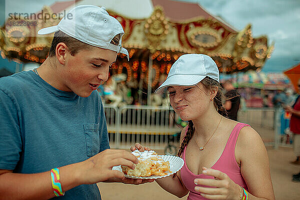 Zwei glückliche Teenager teilen sich auf einem Jahrmarkt einen Trichterkuchen