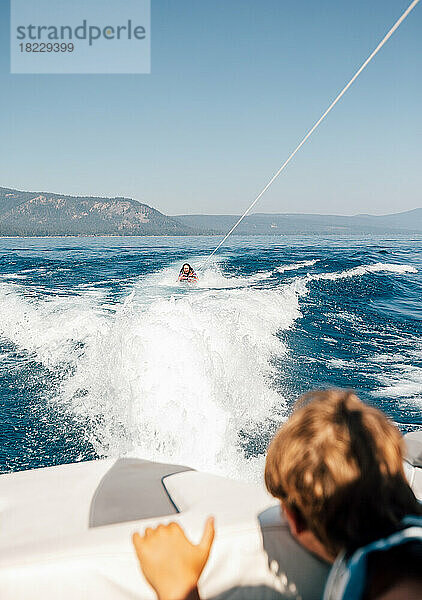 Junge (12-13) schaut Frau beim Wakeboarden zu