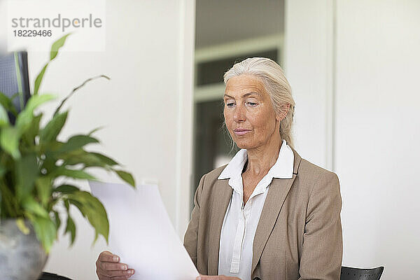 Reife Geschäftsfrau schaut sich Dokument im Büro an
