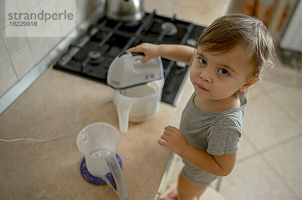 Cute little boy using electric mixer for making pancakes at home