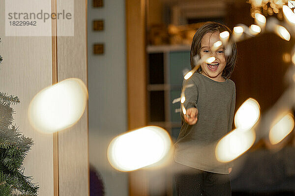 Happy cute boy playing with string light at home