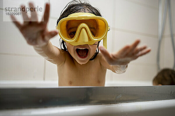Fröhlicher Junge mit Schwimmbrille badet zu Hause im Badezimmer