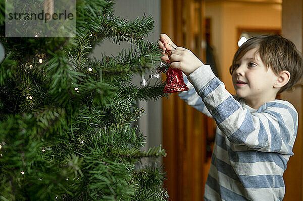 Junge schmückt zu Hause den Weihnachtsbaum