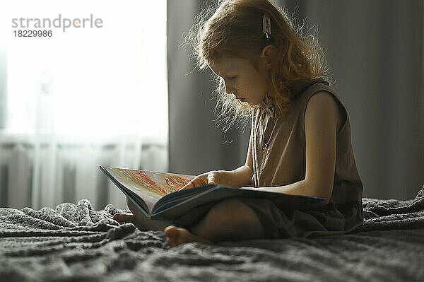 Mädchen liest Buch und sitzt zu Hause im Bett