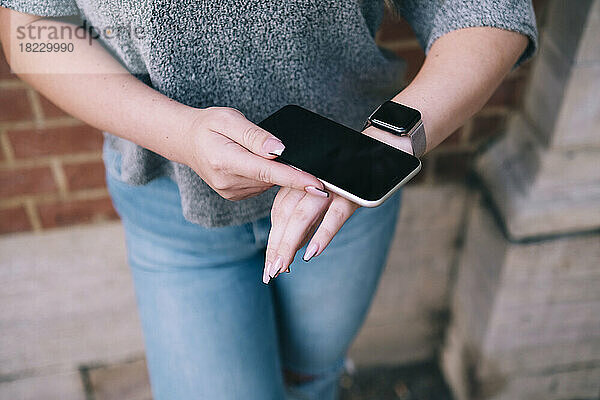 Frau verbindet Mobiltelefon mit Smartwatch und steht vor der Wand