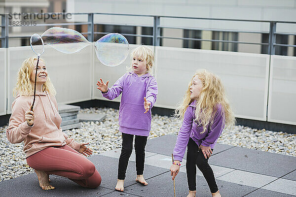 Lächelnde Mutter spielt mit Töchtern auf dem Dach mit Seifenblasenstab