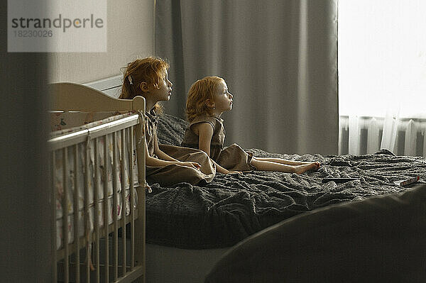 Mädchen mit Schwester sitzt im Bett und schaut zu Hause fern