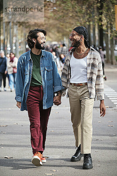 Lächelndes schwules Paar hält sich an den Händen und geht auf der Straße