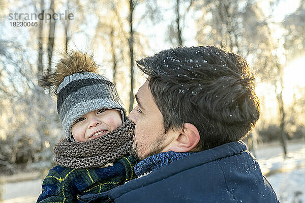 Lächelnder Junge mit Vater in warmer Kleidung im Winterpark