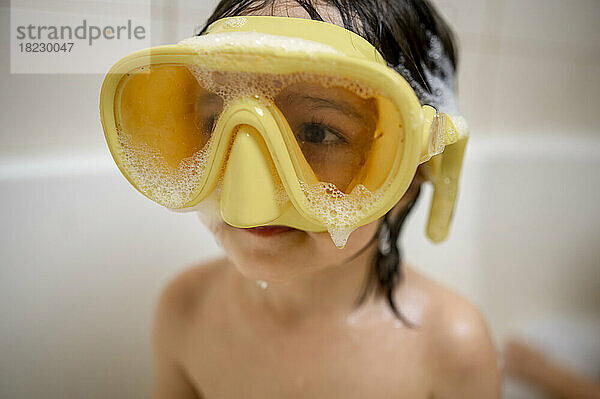 Niedlicher Junge mit gelber Schwimmbrille und Seifenlauge badet im Badezimmer