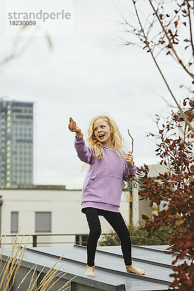 Girl holding stick dancing on rooftop in front of sky