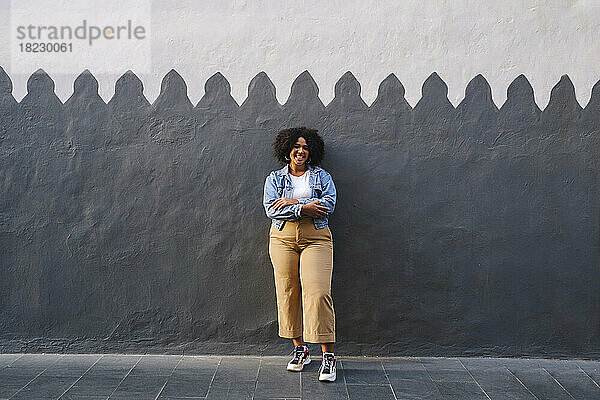 Happy woman with arms crossed standing in front of wall