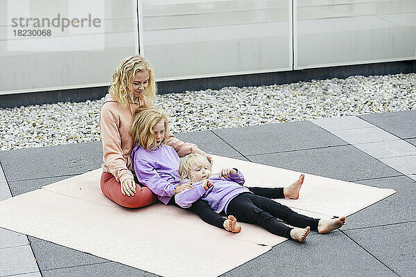 Mädchen liegen mit ihrer Mutter auf einer Gymnastikmatte auf dem Dach