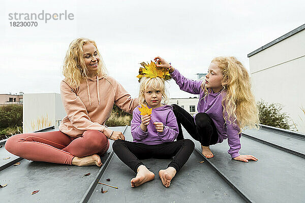 Familie spielt mit Herbstblättern und sitzt zusammen auf dem Dach