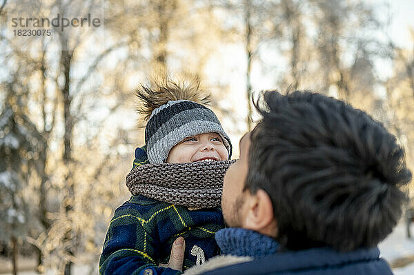 Mann trägt glücklichen Sohn mit Strickmütze im Winter