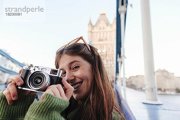 Glückliche junge Frau mit Kamera auf der Tower Bridge  London  England