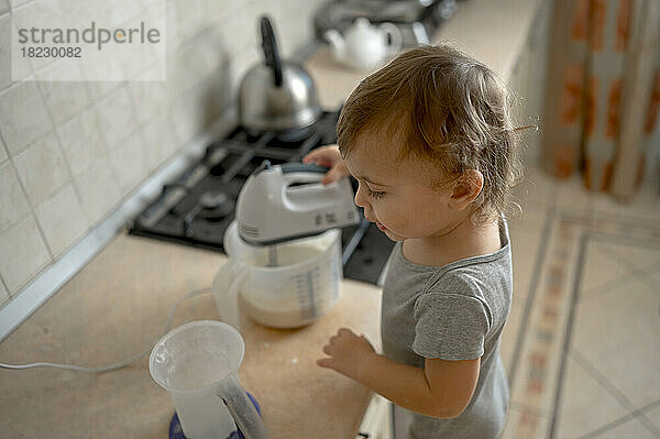 Toddler mixing batter with electric mixer in kitchen at home