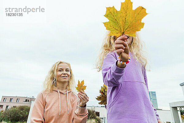 Lächelnde Frau hält das Herbstblatt ihrer Tochter vor dem Himmel