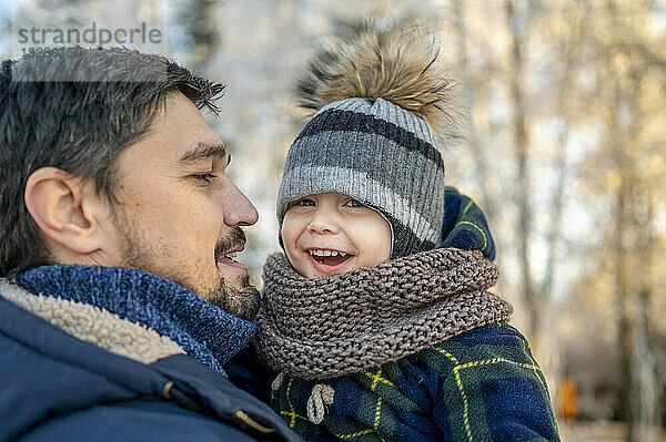 Vater trägt glücklichen Sohn mit Strickmütze im Winter