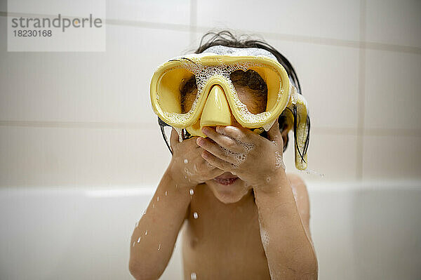 Junge mit gelber Schwimmbrille bedeckt Augen mit Händen im Badezimmer
