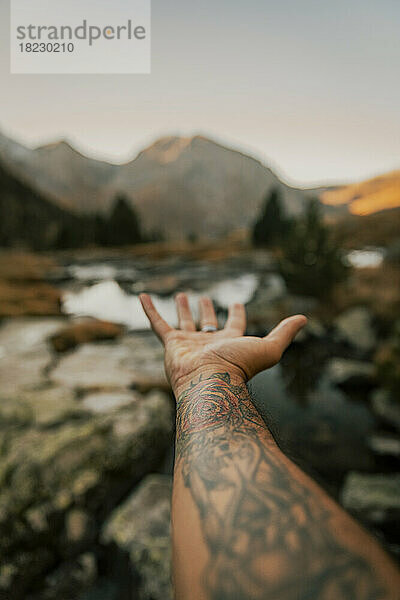 Man with tattooed hand gesturing towards lake