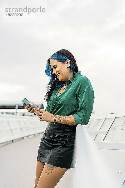 Smiling woman using smart phone leaning by railing