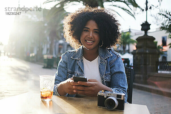Lächelnde Frau mit Smartphone sitzt im Straßencafé