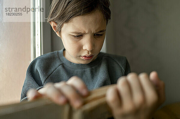 Junge liest Buch am Fenster zu Hause