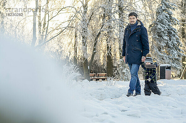 Mann hält die Hand seines Sohnes und geht im Winterpark spazieren