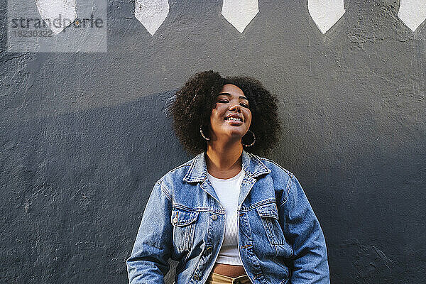Smiling young woman with curly hair in front of wall