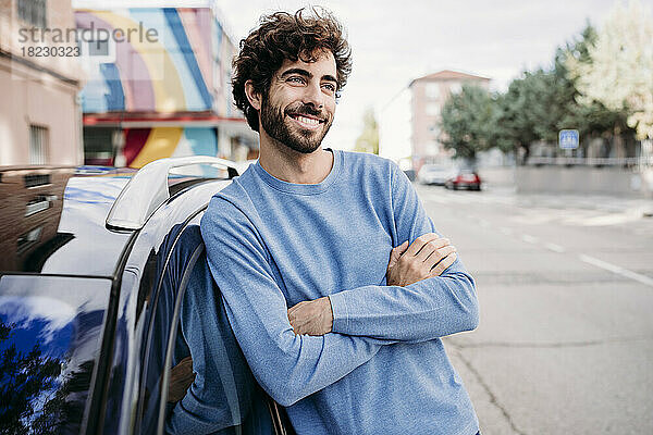 Smiling man with arms crossed day dreaming by car