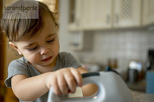 Cute toddler using electric mixer in kitchen at home