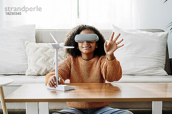 Mädchen mit Virtual-Reality-Simulator sitzt zu Hause mit Windturbinenmodell
