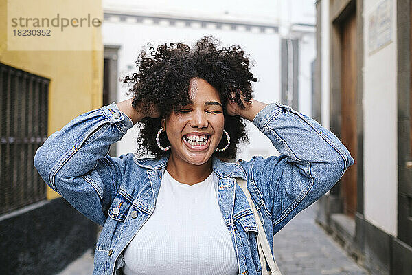 Happy young woman with hands in hair at alley