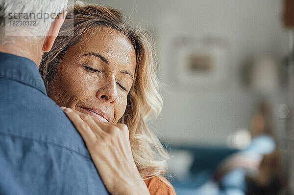 Reife Frau mit geschlossenen Augen umarmt Mann zu Hause