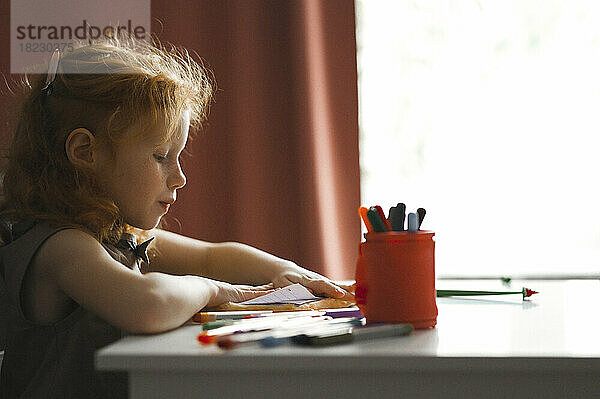 Mädchen zeichnet auf Papier und sitzt zu Hause am Schreibtisch