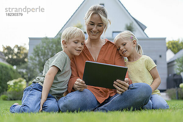 Lächelnde Mutter zeigt Kindern im Hinterhof Tablet-PC