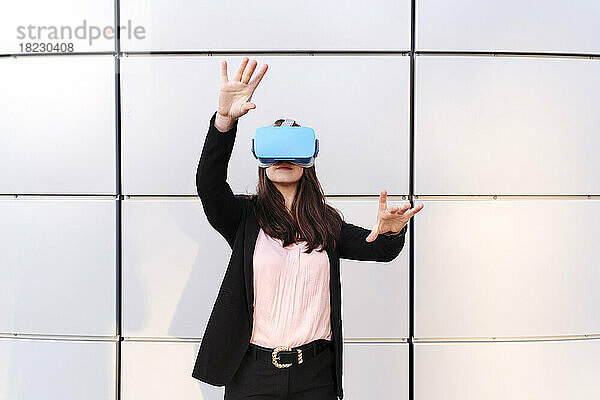 Junge Frau mit Virtual-Reality-Simulator gestikuliert vor der Wand