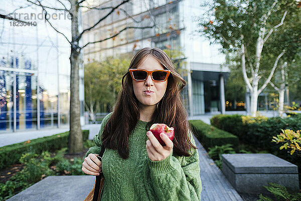 Frau mit Sonnenbrille isst Apfel vor Gebäude