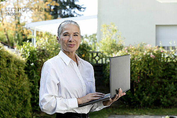 Lächelnde ältere Frau hält Laptop im Garten