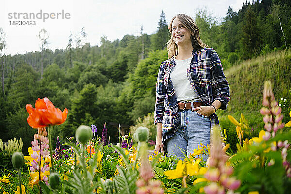 Glückliche junge Frau  die inmitten von Blumen auf dem Feld steht