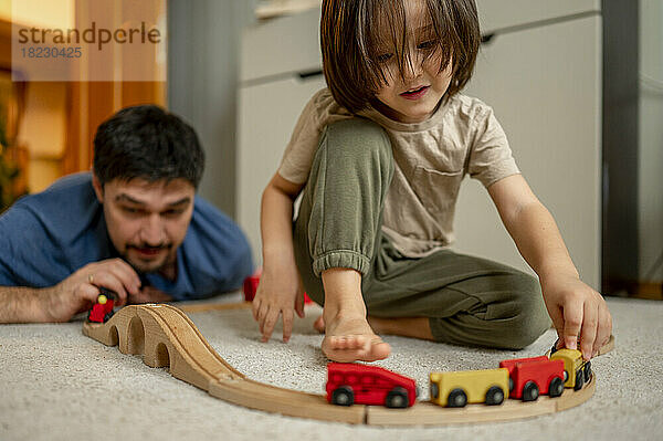 Vater und Sohn spielen zu Hause mit einer hölzernen Spielzeugeisenbahn