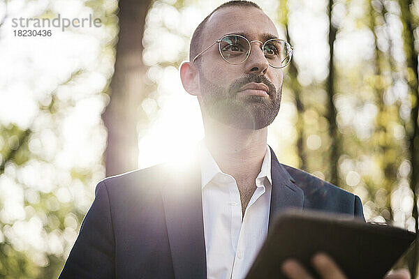 Businessman wearing eyeglasses holding tablet PC on sunny day