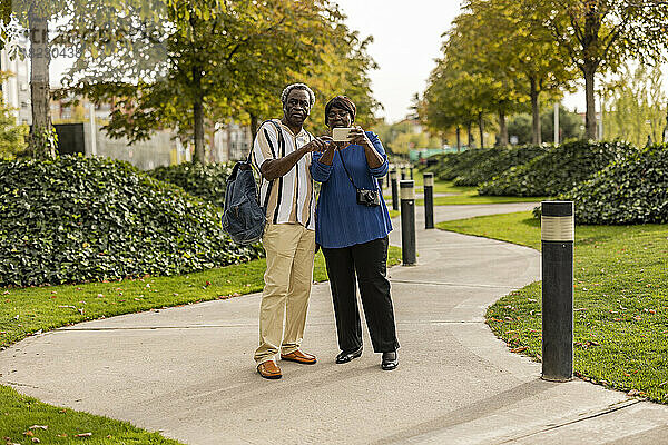 Mann und Frau nutzen Smartphone und stehen auf Fußweg im Park